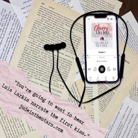 On a backdrop of book pages, an iPhone with the cover of the audiobook of Cherry on Top by Georgia Beers, narrated by Lula Larkin. At the bottom of the image, a pink strip of torn paper with a quote: "You’re going to want to hear Lula Larkin narrate the first kiss." and a url: judeinthestars.com.