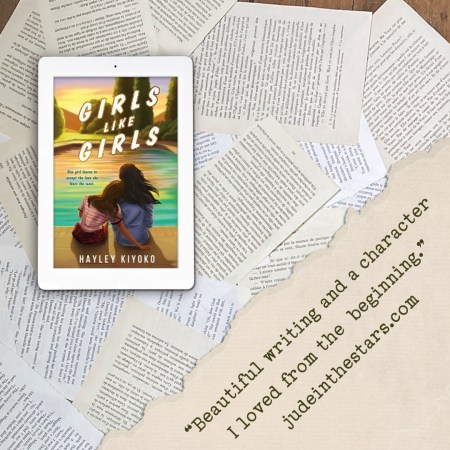 On a backdrop of book pages, an iPad with the cover of Girls Like Girls by Hayley Kiyoko. On the right hand side of the image, a strip of torn paper with a quote: "Beautiful writing and a main character I loved from the beginning." and a URL: judeinthestars.com.