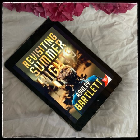 An iPad with the cover of Revisiting Summer Nights by Ashley Bartlett, on a white sheet, with a couple of pink hydrangea flowers near the top of the picture.